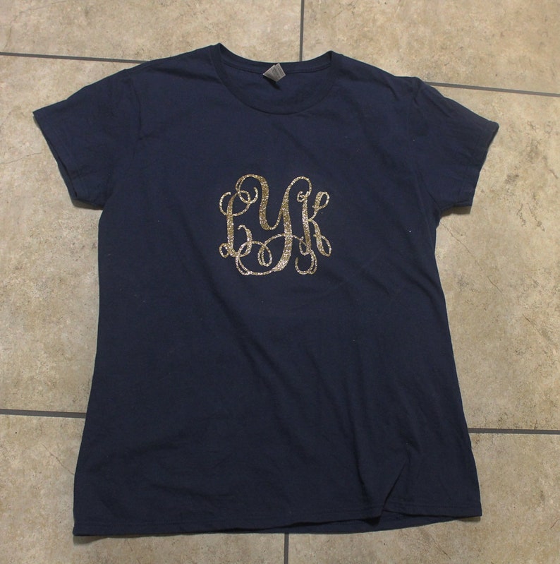 May include: A navy blue t-shirt with a gold glitter monogram of the letters "LYK" on the front.