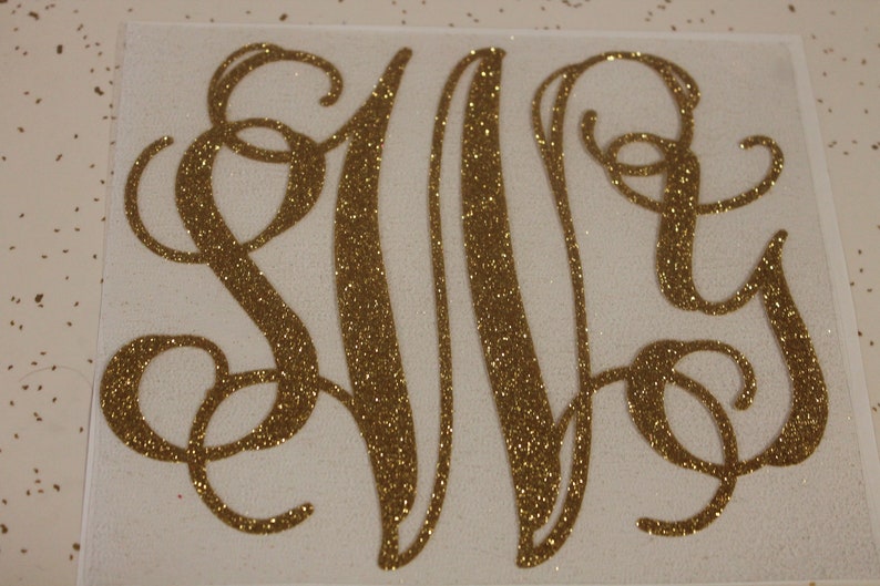 May include: Gold glitter monogram with the letters S, M, and Y in a cursive script font.