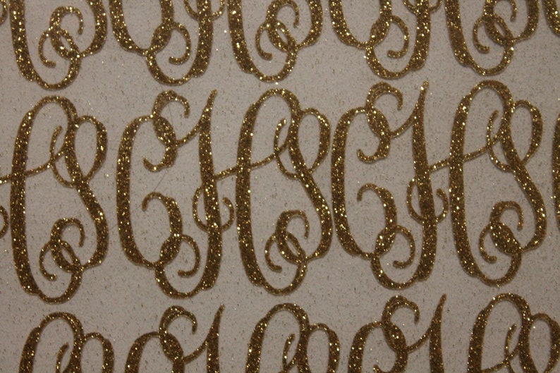 May include: A close-up of a sheet of gold glitter paper with multiple cut-out letters in a cursive font. The letters are all the same, and they are arranged in a random pattern.