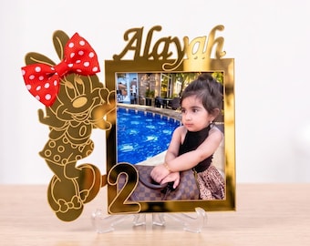 May include: A gold-toned acrylic photo frame featuring a cutout of a cartoon mouse character with a red and white polka dot bow. The frame displays the name Alayah in script at the top and the number 2 at the bottom, holding a photo of a child.