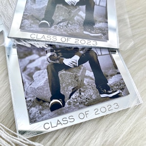 Puede incluir: Un marco de espejo plateado con una foto en blanco y negro de una persona sentada en rocas. El marco tiene el texto "Class of 2023" en la parte inferior.