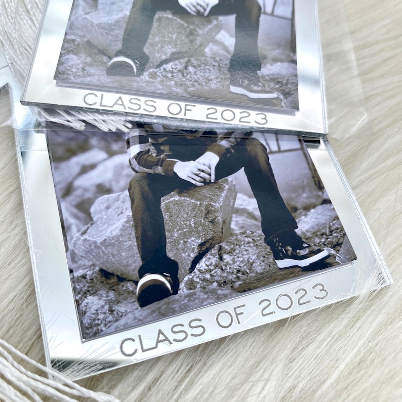 Puede incluir: Un marco de espejo plateado con una foto en blanco y negro de una persona sentada en rocas. El marco tiene el texto "Class of 2023" en la parte inferior.
