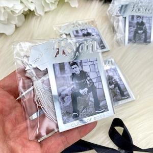 Puede incluir: Marco de fotos plateado para graduaci&oacute;n con un borla blanca y una foto en blanco y negro de un graduado. El marco tiene el nombre "Ryan" y el texto "Clase de 2023". El marco tambi&eacute;n tiene la fecha "17 de junio de 2023".