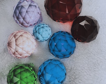 May include: A collection of faceted crystal spheres in various colors, including red, purple, blue, green, and pink. The spheres are arranged on a soft, white surface. The text "Ping's gifts Inc" is visible at the bottom.