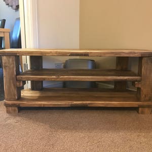 Op de afbeelding: Een rustieke houten tv-standaard met twee planken. De standaard is gemaakt van lichtbruin, gerecycled hout en heeft een eenvoudig, stevig ontwerp. De standaard is ongeveer 122 cm breed, 46 cm diep en 51 cm hoog.