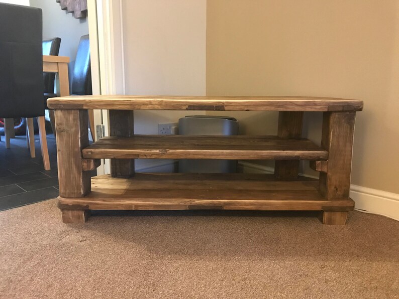 Op de afbeelding: Een rustieke houten tv-standaard met twee planken. De standaard is gemaakt van lichtbruin, gerecycled hout en heeft een eenvoudig, stevig ontwerp. De standaard is ongeveer 122 cm breed, 46 cm diep en 51 cm hoog.