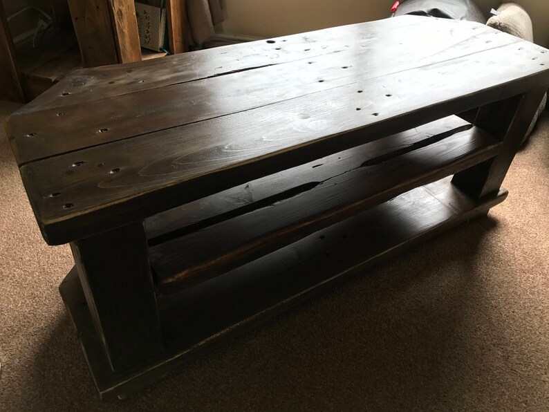 Op de afbeelding: Een donker gebeitste houten salontafel met twee planken. De tafel is rechthoekig met een lattenbovenkant en is gemaakt van dikke houten planken. De tafel is ongeveer 122 cm lang, 51 cm breed en 46 cm hoog.