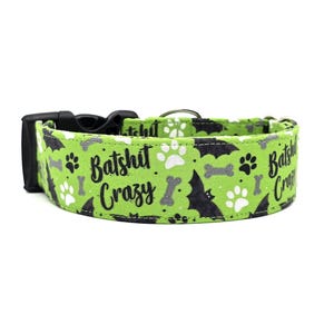 May include: A green dog collar with a black plastic buckle. The collar features a repeating pattern of black bats, paw prints, and bones on a green background. The words "Batshit Crazy" are printed on the collar in black.