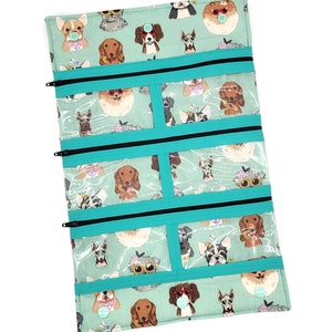 Peut inclure: Une pochette zippée turquoise avec des fenêtres en plastique transparent. La pochette est ornée d'un motif imprimé de chiens de différentes races portant des lunettes de soleil et des chapeaux. La pochette comporte plusieurs compartiments et est parfaite pour organiser de petits objets.