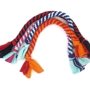 May include: Four colorful braided dog toys with knotted ends. The toys are made of woven fabric in black and red, pink and blue, purple and white, and orange and red.