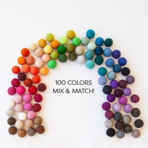 May include: A collection of 100 colorful felt balls arranged in a rainbow arc. The balls range in color from reds and oranges to greens, blues, and purples. The text "100 COLORS MIX & MATCH!" is displayed below the balls.
