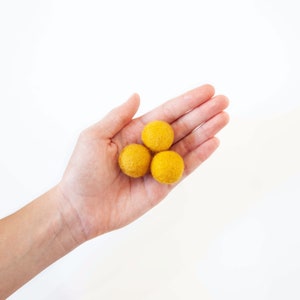 Hand showing the relative size of Wool Mob's Small felt balls. Each measures 2.5 cm or roughly 1 inch in diameter. Color shown is Sunrise or a rich, bright yellow.