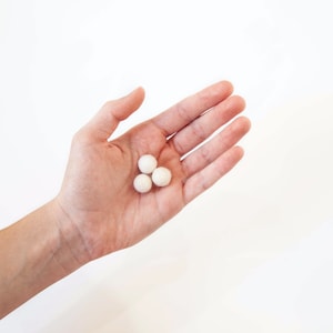 Hand showing the relative size of Wool Mob's mini felt balls. Each measures roughly 1 cm or 0.4 inches in diameter. Hand is holding Snow felt balls which are white in color.