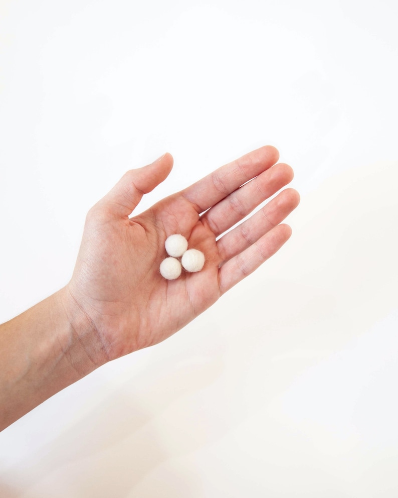 Hand showing the relative size of Wool Mob's mini felt balls. Each measures roughly 1 cm or 0.4 inches in diameter. Hand is holding Snow felt balls which are white in color.