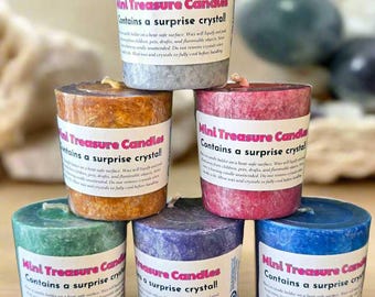 May include: A stack of six mini treasure candles in various colors: gray, orange, pink, green, purple, and blue. Each candle has a label that reads "Mini Treasure Candles Contains a surprise crystal!"