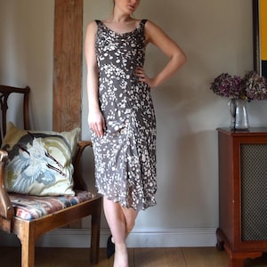 May include: A brown sleeveless dress with a white floral print. The dress has a cowl neck and a flowing skirt.