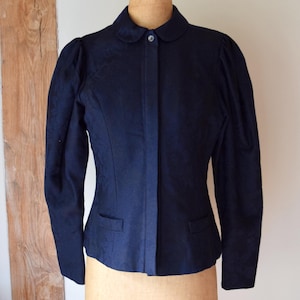 Op de afbeelding: Een marineblauwe jas met een ronde kraag en kleine zakken. De jas heeft lange mouwen met pofmouwen en een enkele knoopsluiting. De jas wordt getoond op een vintage paspop.