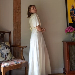 May include: A white maxi dress with a long skirt and short sleeves. The dress has a V-neckline and a tie at the waist. The dress is made of a soft, flowing fabric.