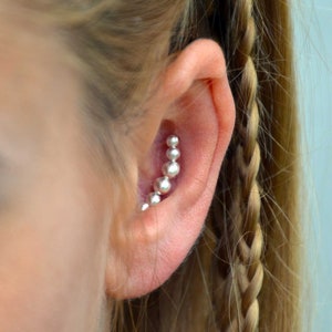 May include: A close-up of a woman's ear with a row of small, white pearl-like beads in a helix piercing.