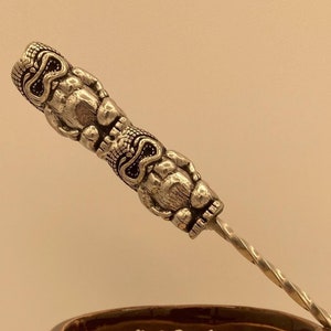 May include: A brown ceramic tiki mug with a pineapple design and white rice inside. A silver metal tiki-shaped stirrer is resting on the rim of the mug.