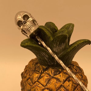 May include: A gold pineapple skull with a silver cocktail stirrer sticking out of the top.