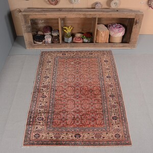 May include: A rectangular area rug featuring a central field of intricate floral patterns in shades of terracotta, rust, and cream. The rug is framed by a wide, detailed border with repeating botanical motifs in navy blue, beige, and soft pink tones.