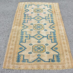 May include: A rectangular area rug featuring a tan background with a central geometric pattern in blue. The design includes three large octagonal medallions with floral motifs, surrounded by smaller flower shapes and a stepped border with fringe.