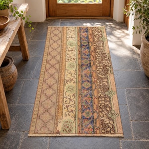 Peut inclure: Un tapis rectangulaire au design patchwork composé de bandes verticales dans des tons marron, beige, bleu et vert. Le motif présente des formes géométriques quadrilobées, des motifs floraux et une bordure grecque, avec des franges aux extrémités.