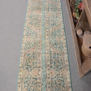 May include: A long, rectangular rug with a teal border and a beige and teal patterned design. The rug has a traditional, vintage look.