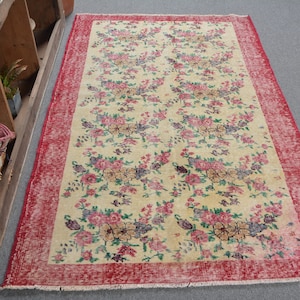 Puede incluir: Una alfombra vintage con estampado floral y borde rojo. La alfombra tiene un fondo crema con diseños florales rosas, amarillos y verdes.