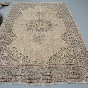 May include: A rectangular area rug featuring a beige field with a central dark gray medallion and intricate floral patterns. The rug is framed by a wide, detailed border in shades of gray and brown, finished with short fringe along the edges.