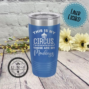 May include: A blue stainless steel tumbler with a white design that says "This is my circus. These are my monkeys." The tumbler has a lid and is laser etched.