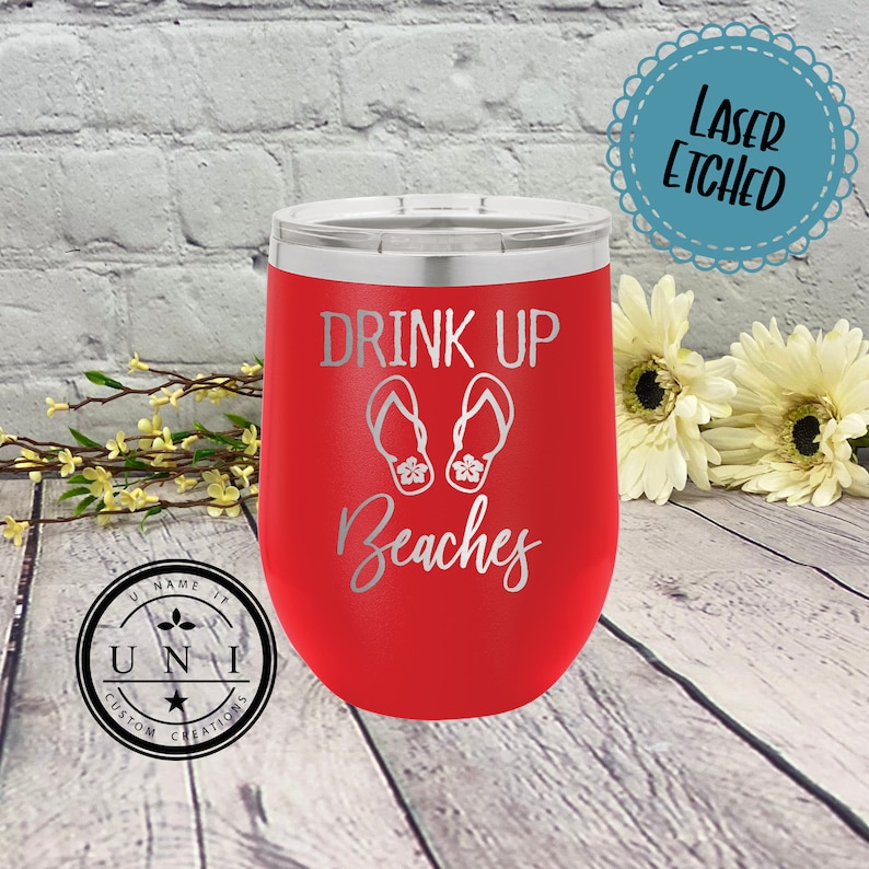 May include: Red stainless steel wine tumbler with a white laser etched design that says "Drink Up Beaches" with a pair of flip flops.