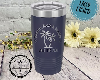 May include: Navy blue insulated tumbler with a silver lid. The tumbler features the text "Beaches, Booze & Besties" and "GIRLS TRIP 2024" with a palm tree graphic. The words "LASER ETCHED" are also visible.