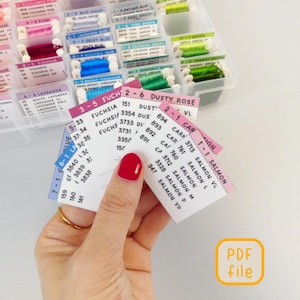 May include: A hand holds colour swatch cards with thread colour codes and names, including "Dusty Rose" and "Fuchsia." The cards are in front of a clear plastic organiser filled with spools of colourful embroidery floss. A "PDF file" icon is in the corner.