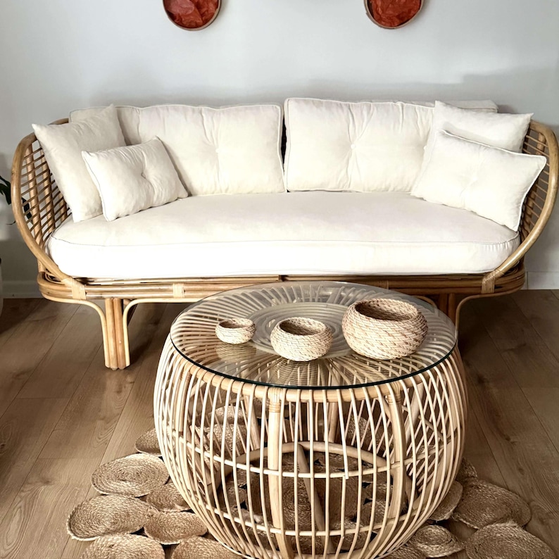 May include: A white wicker sofa with white cushions and a round wicker coffee table with a glass top. Three small woven baskets are on the table.