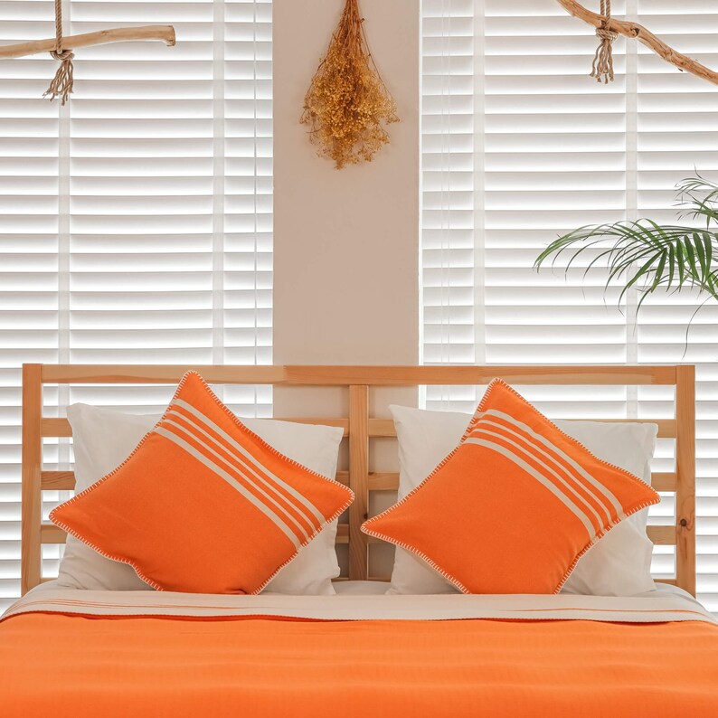May include: A wooden bed frame with a white and orange striped pillow on each side. The bed is made with a white sheet and an orange blanket.