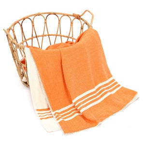May include: An orange and white striped throw blanket with a white crocheted border, draped over a wicker basket.