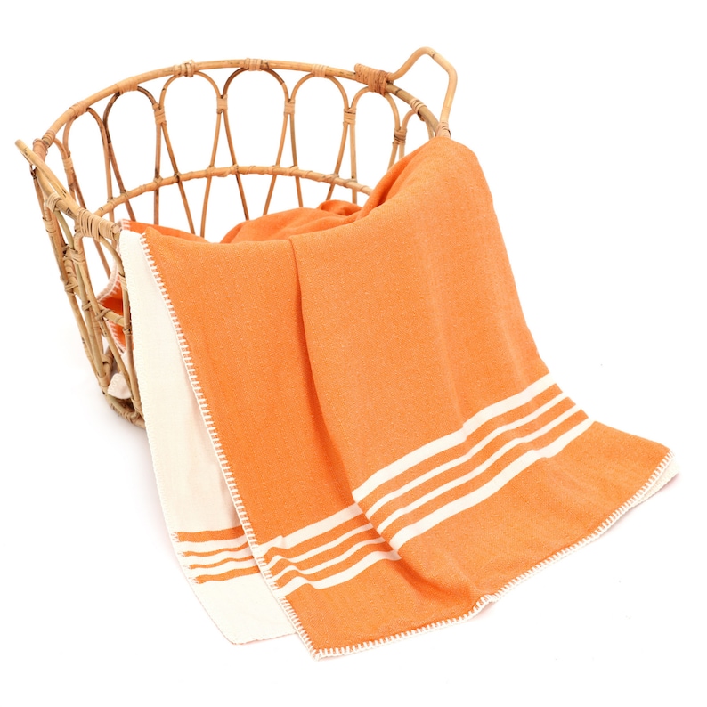 May include: An orange and white striped throw blanket with a white crocheted border, draped over a wicker basket.