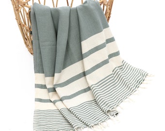 May include: A soft, striped, green and white cotton throw blanket with fringe. The blanket is folded and draped over a wicker basket.
