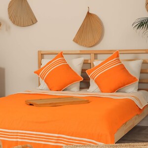 May include: A bed with a bright orange duvet cover and white stripes. Two orange pillows with white stripes are on the bed. The bed is made of wood and has a wooden headboard.