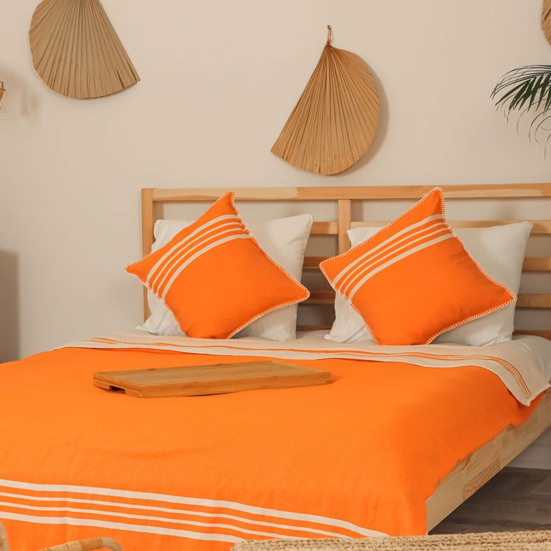 May include: A bed with a bright orange duvet cover and white stripes. Two orange pillows with white stripes are on the bed. The bed is made of wood and has a wooden headboard.