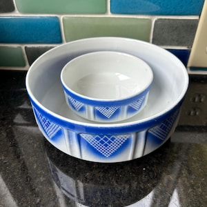 May include: Two white ceramic bowls with a blue geometric design. The larger bowl contains a smaller bowl. The bowls have a white interior and a blue patterned exterior. The design features a series of diamond shapes.