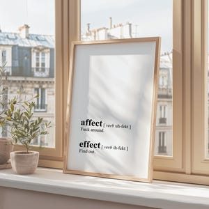 Puede incluir: Una impresión enmarcada con las palabras "affect" y "effect" definidas de forma humorística. La impresión está colgada en una pared frente a una ventana con vista a una ciudad.