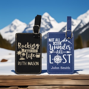 May include: Two personalized leather luggage tags. The black tag says "Rocking the Retired Life" with palm trees and a cocktail glass. The blue tag says "Not all who wander are lost" with a compass and mountains.