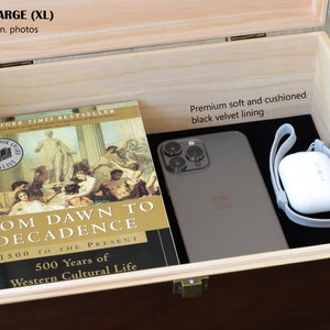 Pu&ograve; includere: Scatola di legno aperta con esterno marrone scuro e interno in legno chiaro. All'interno, un libro intitolato "From Dawn to Decadence" e uno smartphone poggiano su una fodera in velluto nero. &Egrave; visibile anche una custodia bianca per auricolari wireless.
