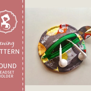 May include: A round gray and yellow fabric headset holder with a zipper closure and a loop for hanging. The holder has a floral pattern and the text "My Little Sewing Monkey" is printed on the fabric.