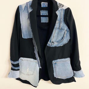 May include: A black blazer with light blue denim patches and pockets. The denim is distressed, and the blazer has denim accents on the sleeves, front, and shoulders. The garment has a unique, patchwork design.