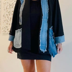May include: A black blazer featuring light blue denim panels with frayed edges along the front lapels and pockets, paired with a black mini dress, a round pendant necklace, and black footwear, creating a layered look with contrasting textures.