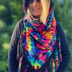 Peut inclure: Une écharpe en polaire à col roulé tie-dye colorée avec des franges noires. L'écharpe a une capuche et est faite d'un matériau doux et chaud.